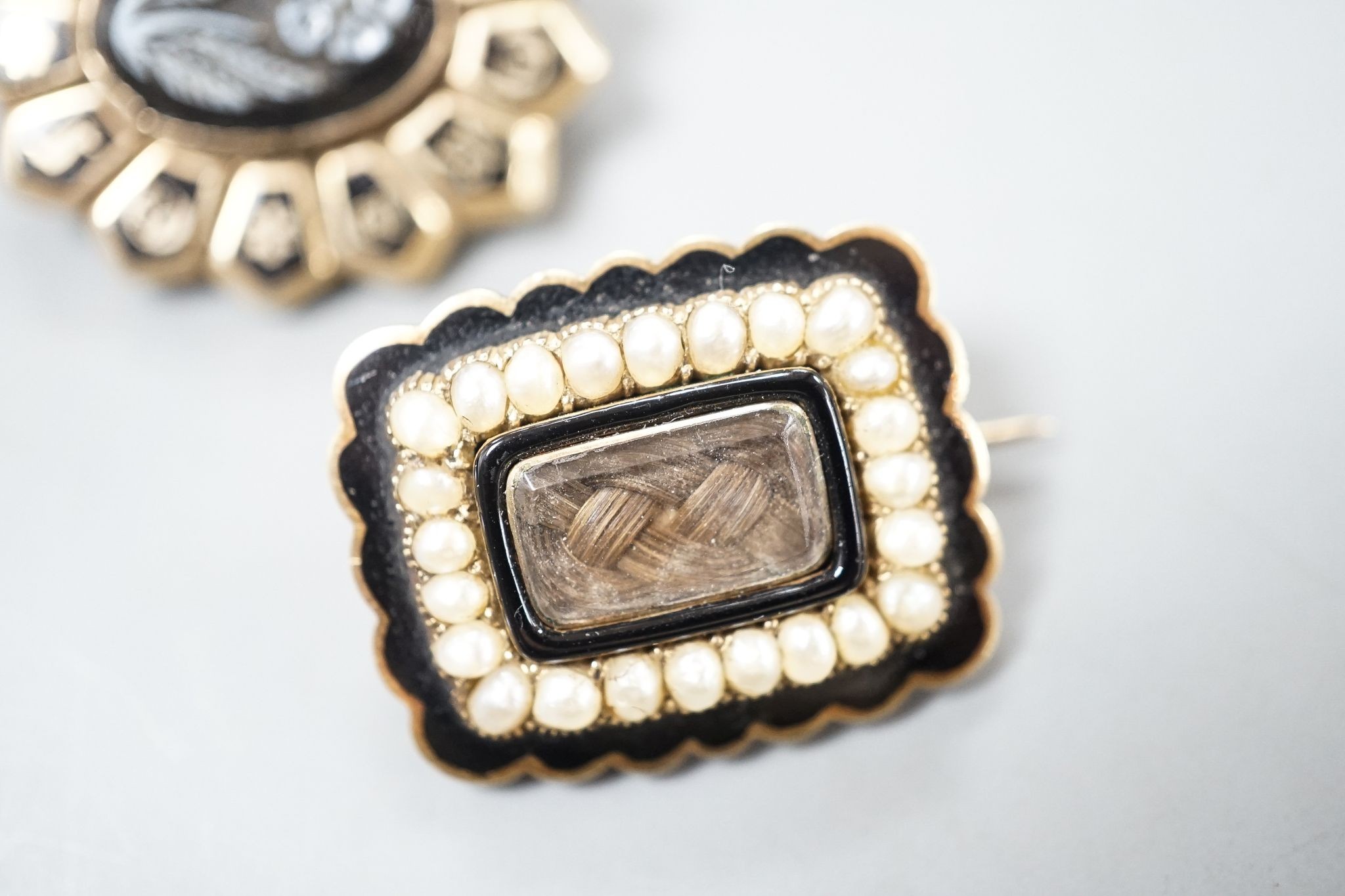 Two 19th century yellwo metal mourning brooches, one with plaited hair, split pearls and engraved inscripotion, the other with sardonyx centre stone, largest 27mm.